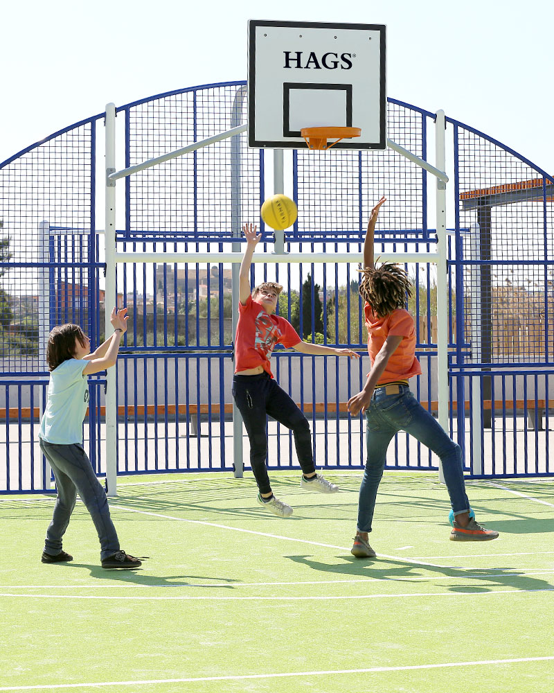 Children play basketball at a MUGA arena.